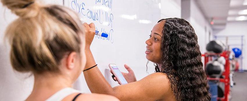 Student writing on white board with another student looking on.